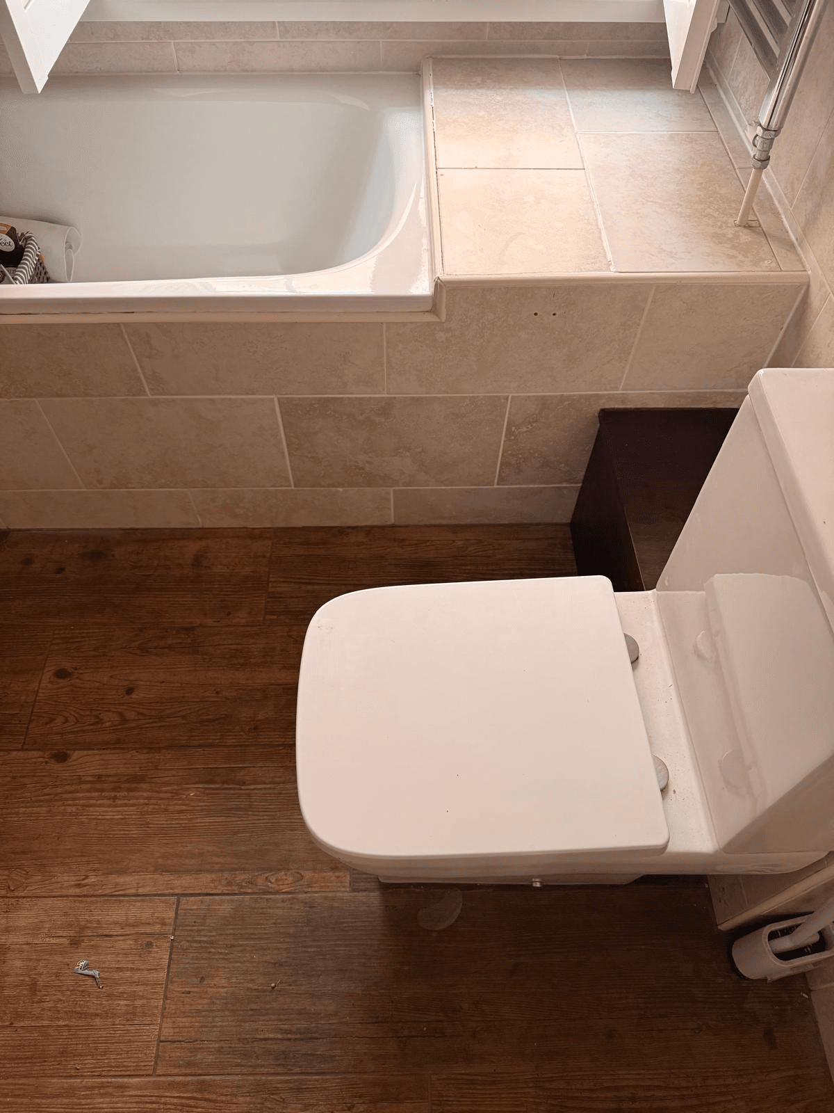 Completed bathroom with tiled surround, fitted bath and wood-effect floor